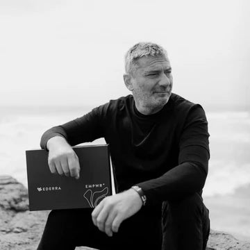 Black and White photo of CEO Vladi Delsoglio Sitting on a cliff by the ocean with a box of EDERRA EMPWR+ Starter Kit facing away from the camera