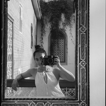 A black and white photo of EDERRA Creative Director Nicole Lewis taking a photo in a mirror with a camera