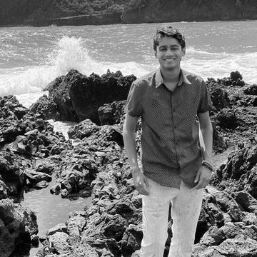 A black and white photo of EDERRA CSO Ruchit Mehta standing on a rocky beach with waves crashing in the background