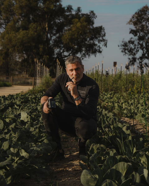 CEO Vladi Delsoglio Crouched in a Field on a Farm with a Biophotonic Jar of EMPWR+ Looking Directly Into the Camera